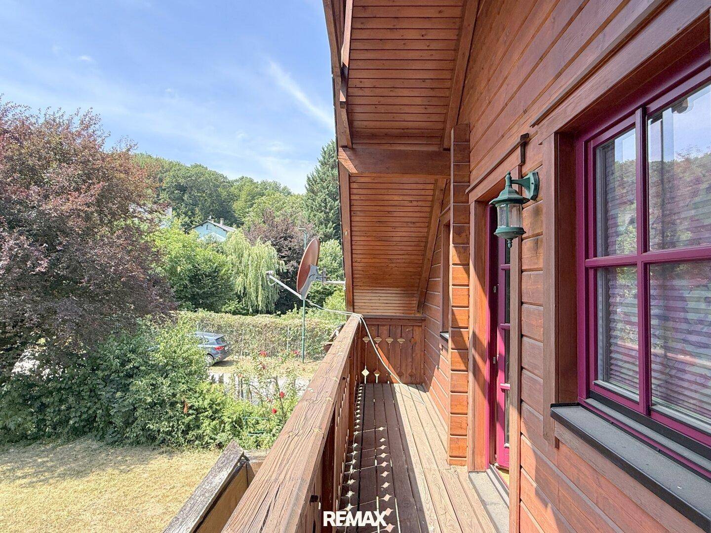 Langer Holzbalkon entlang der Fassade mit Blick auf den Garten und die Umgebung.