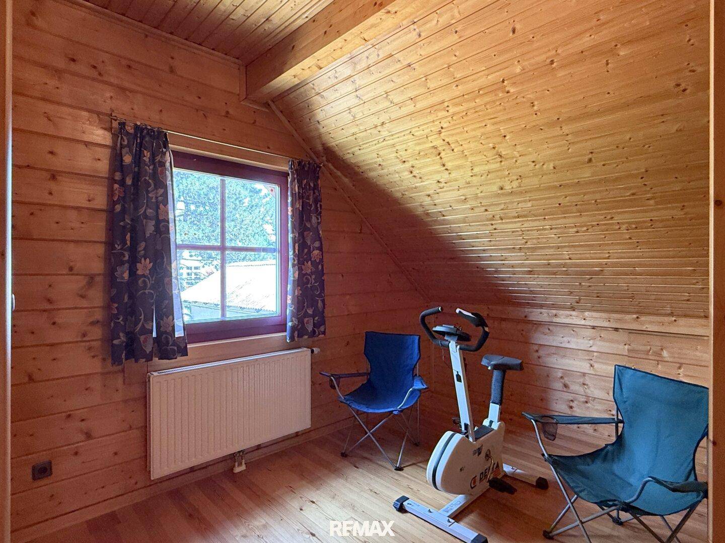 Dachzimmer mit Holzwänden, Holzboden und einem Heimtrainer für sportliche Aktivitäten.