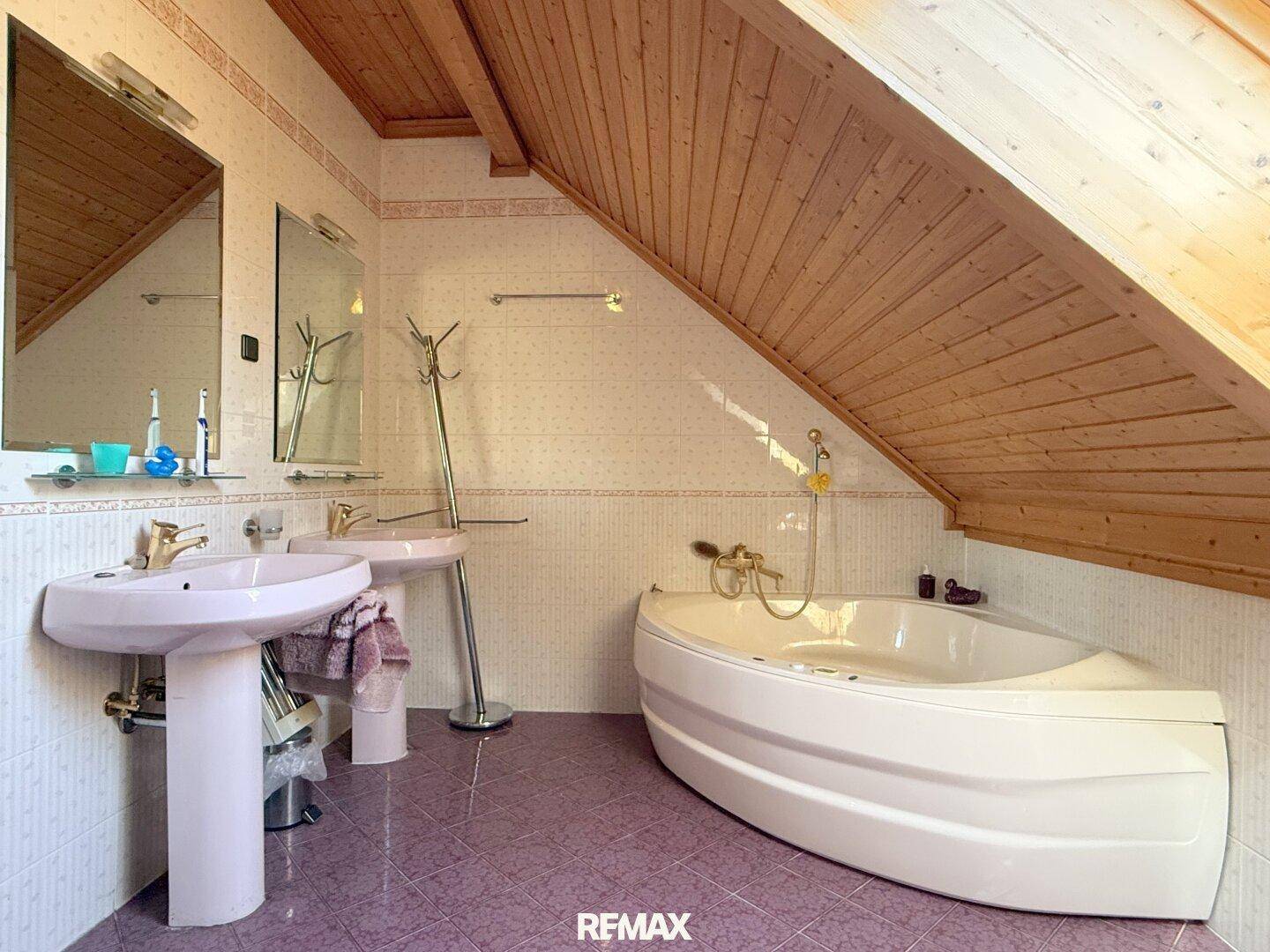 Badezimmer im Dachgeschoss mit Badewanne, Doppelwaschbecken und schräger Holzdecke.