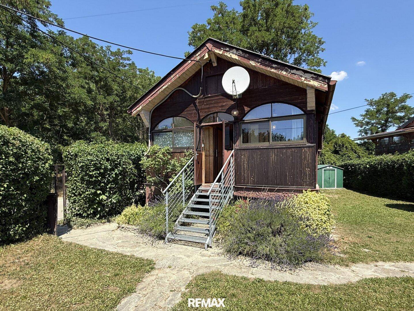 Charmantes Holzhaus mit Metalltreppe und gepflegtem Gartenbereich an einem sonnigen Tag.