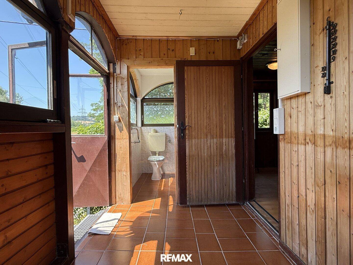 Heller Wintergarten mit Fliesenboden und Zugang zu einer kleinen Toilette mit Fenster.