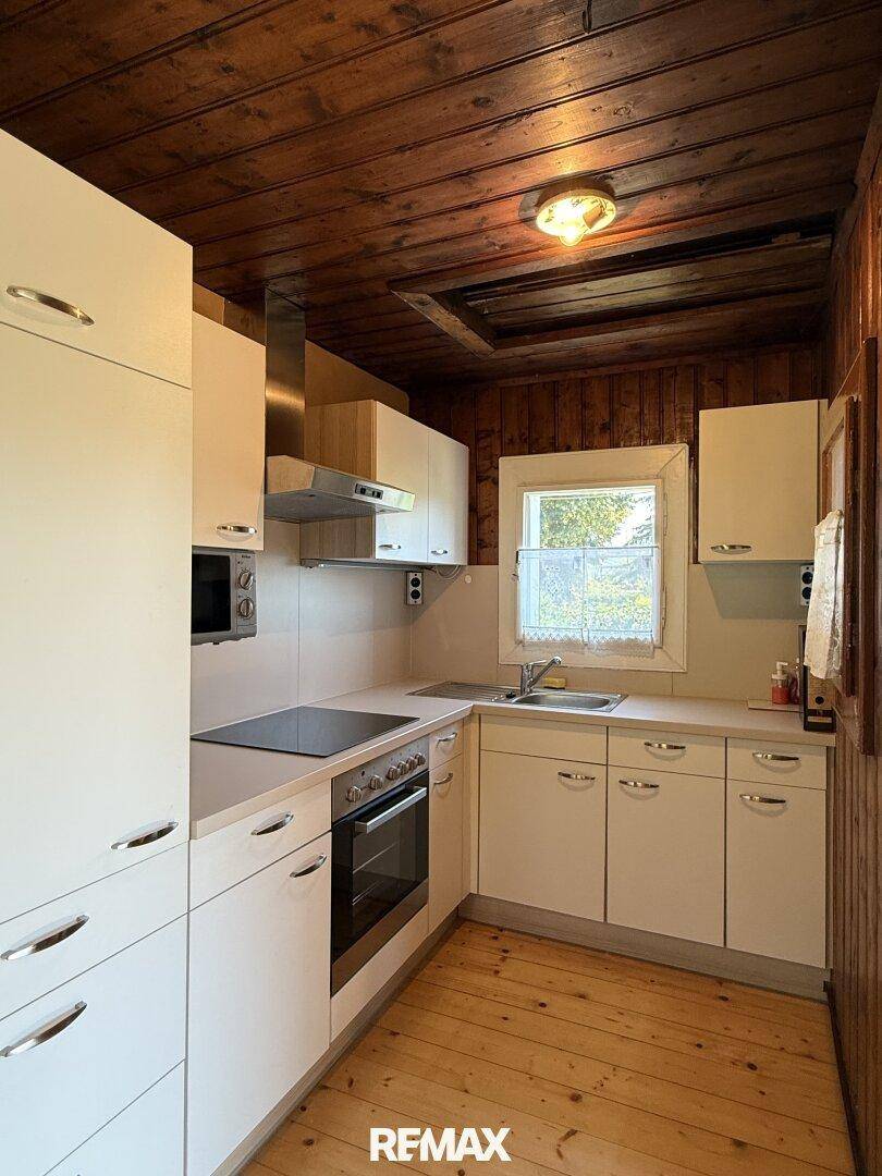 Kleine Küche mit weißen Einbauschränken, Holzdecke und Holzboden in rustikalem Stil.