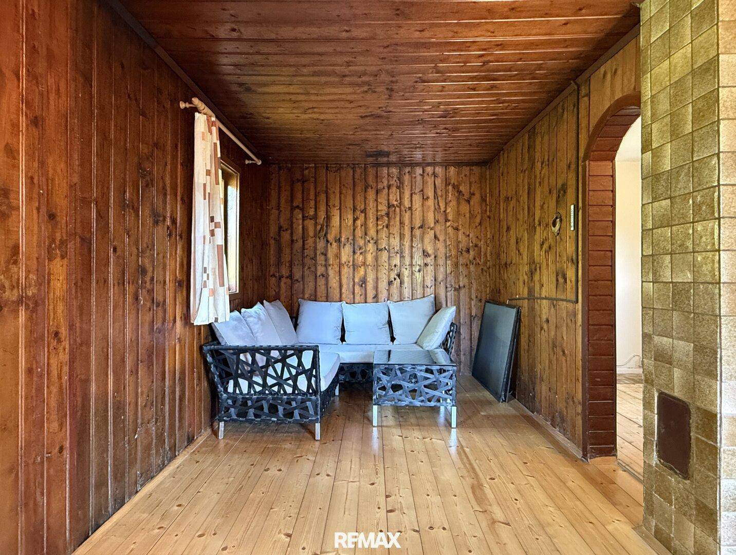 Gemütliches Wohnzimmer mit Holzwänden, Holzdecke und Holzboden, eingerichtet mit einem Sofa.