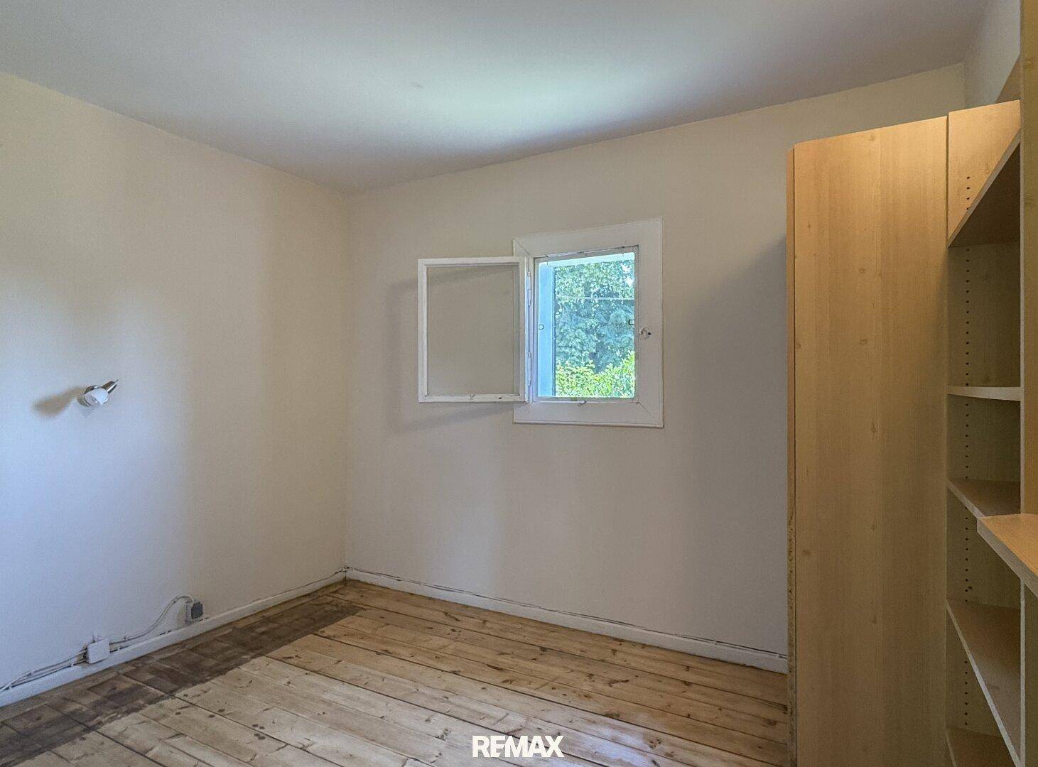 Schlafzimmer mit Holzboden, hellen Wänden und einem offenen Kleiderschrank mit Regalen.