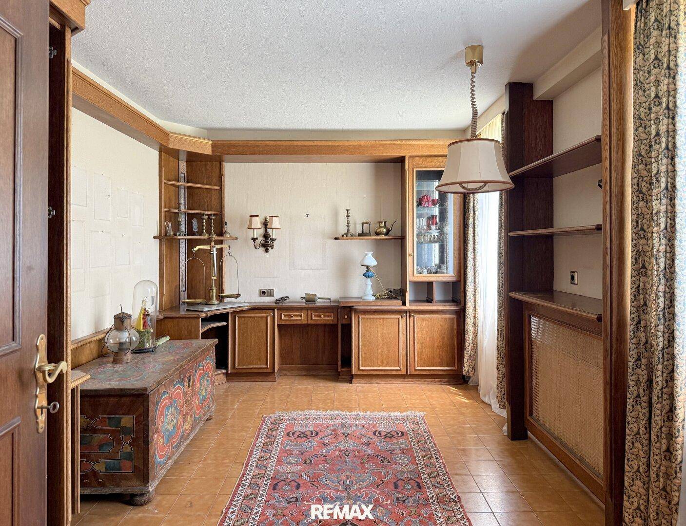 Arbeitszimmer mit Einbauschränken aus Holz, Fliesenboden und traditionellem Teppich.