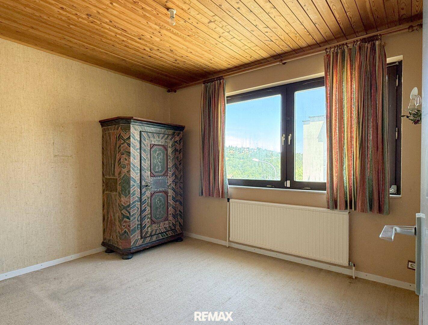Schlafzimmer mit Holzdecke, Teppichboden und großem Fenster mit Ausblick.