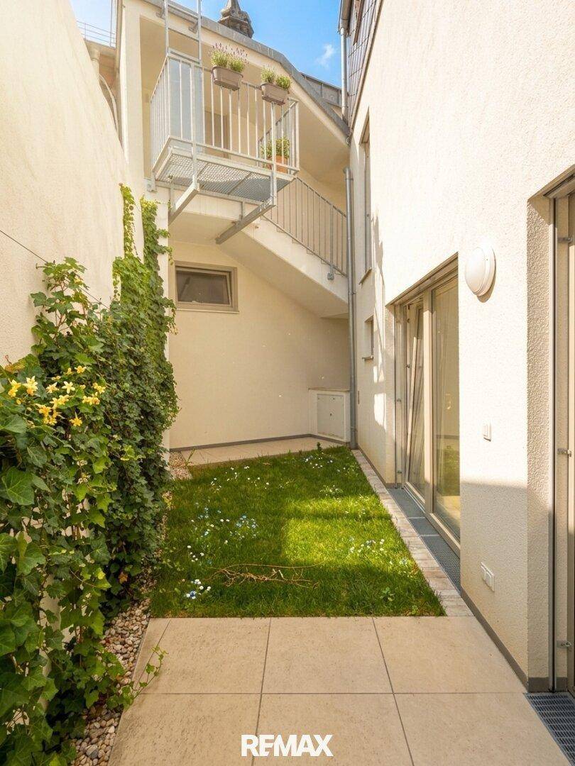 Kleiner, gepflasterter Gartenbereich mit Grünfläche und Außentreppe zu oberen Etagen.