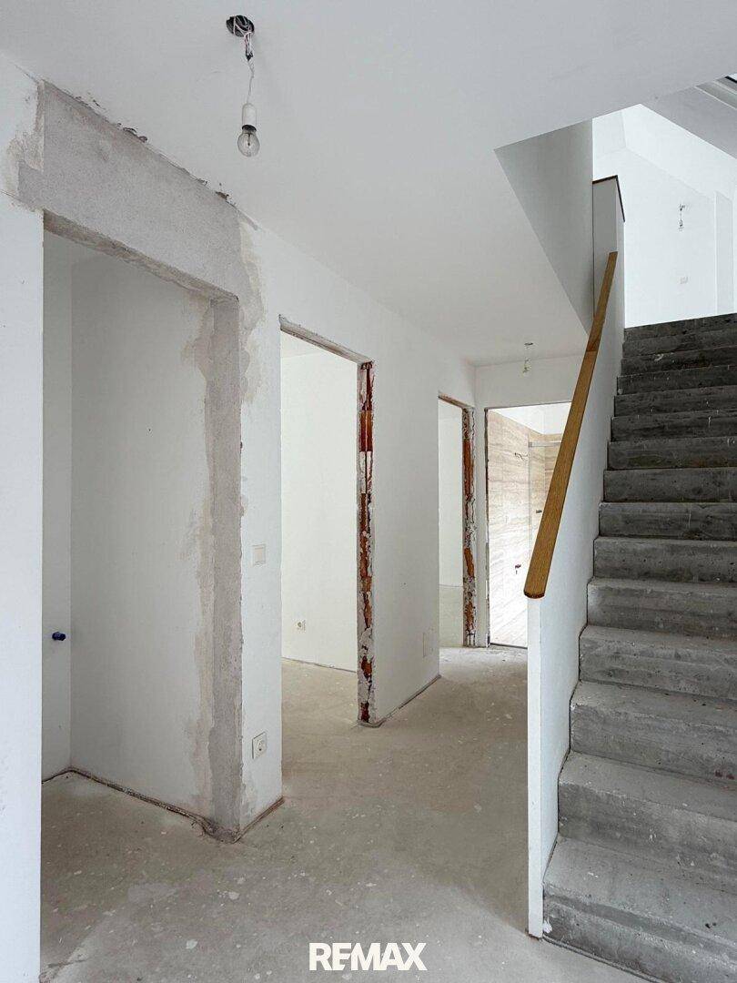 Eingangsbereich im Rohbau mit Treppe und offenen Türrahmen, bereit zur Fertigstellung.