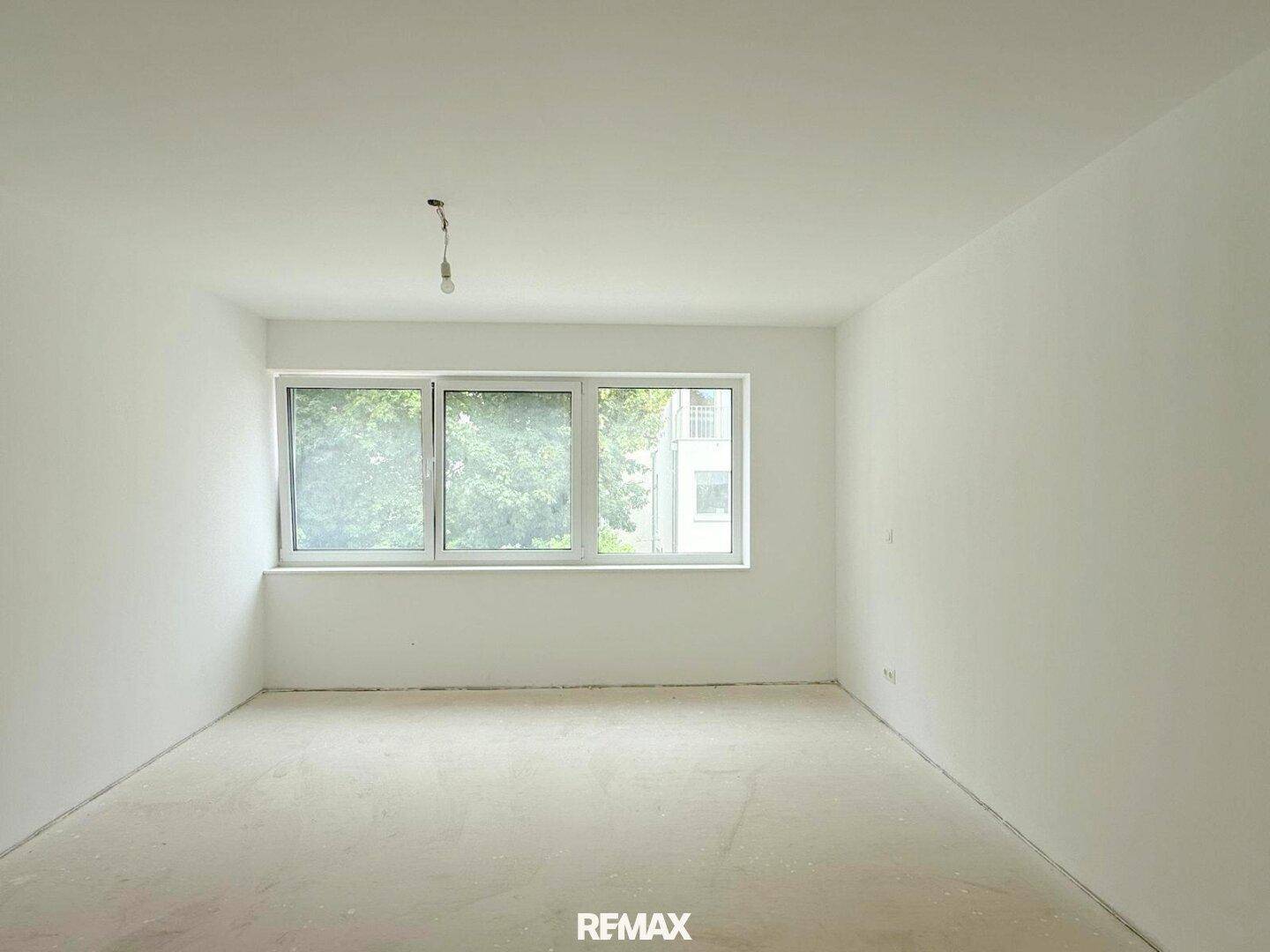 Helles Schlafzimmer im Rohbau mit großem Fenster und Blick ins Grüne.