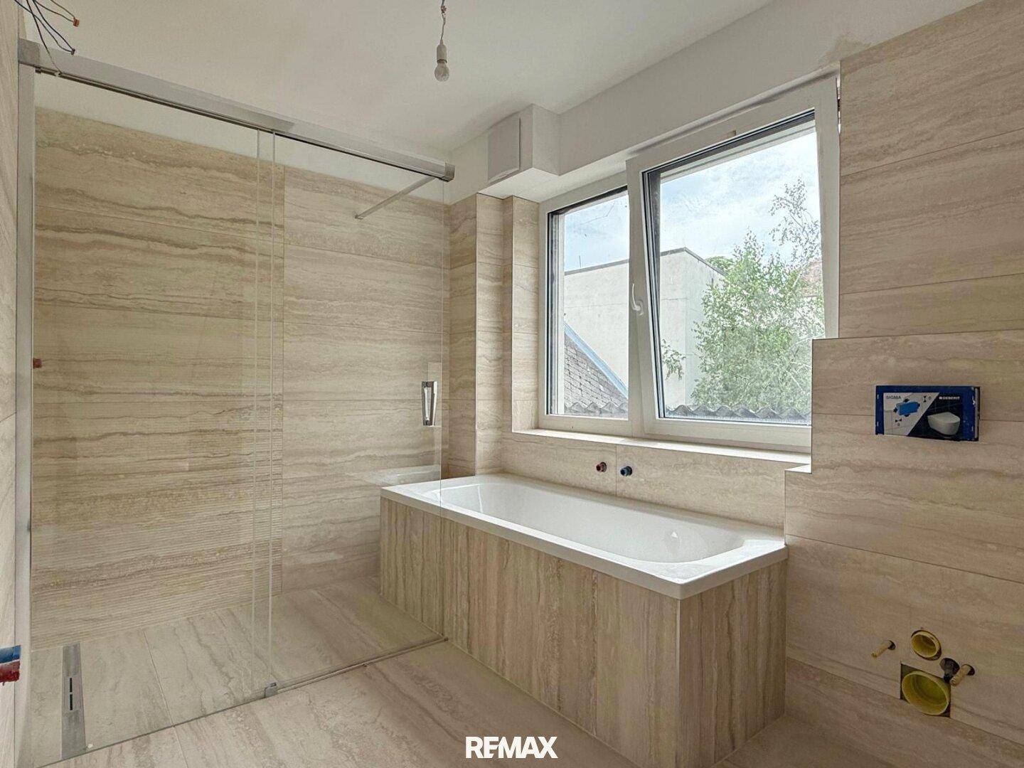 Modernes Badezimmer im Rohbau mit Badewanne, Duschbereich und Fenster.