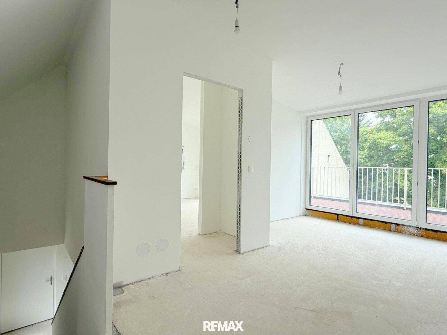Heller Wohnbereich im Rohbau mit Zugang zu einem Balkon und viel Tageslicht.