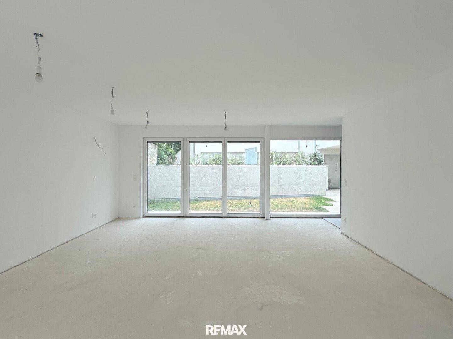 Helles Wohnzimmer im Rohbau mit großen Schiebetüren, die Zugang zum Außenbereich bieten.