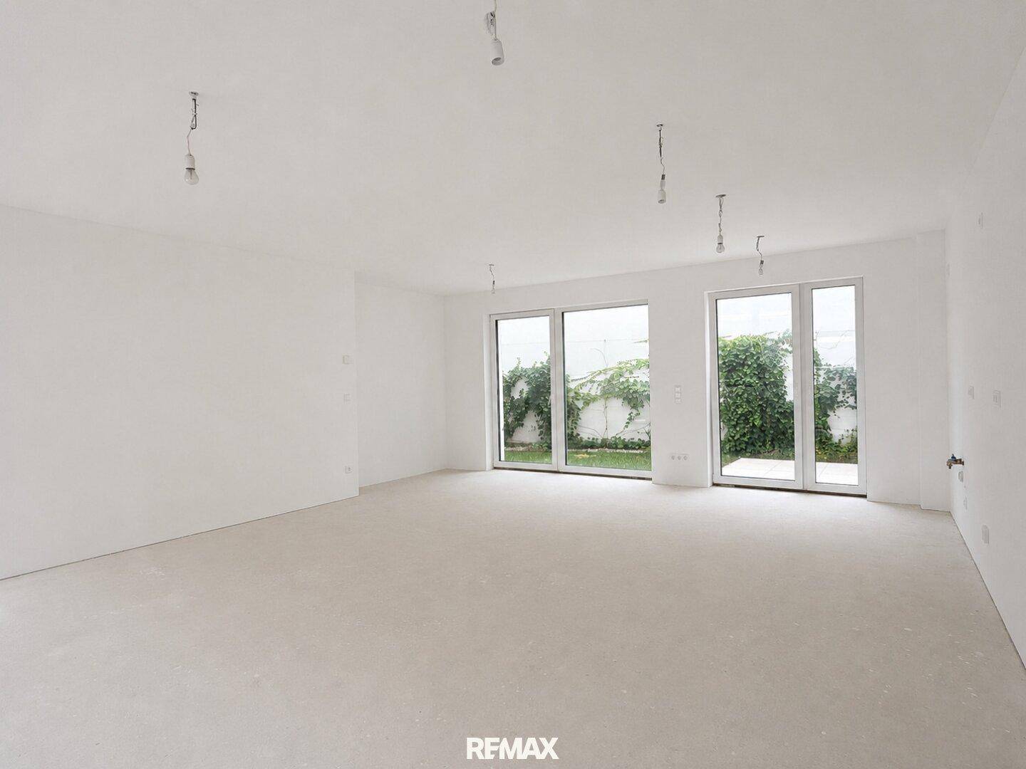 Großes, helles Wohnzimmer im Rohbau mit Blick ins Grüne durch die breiten Fenster.