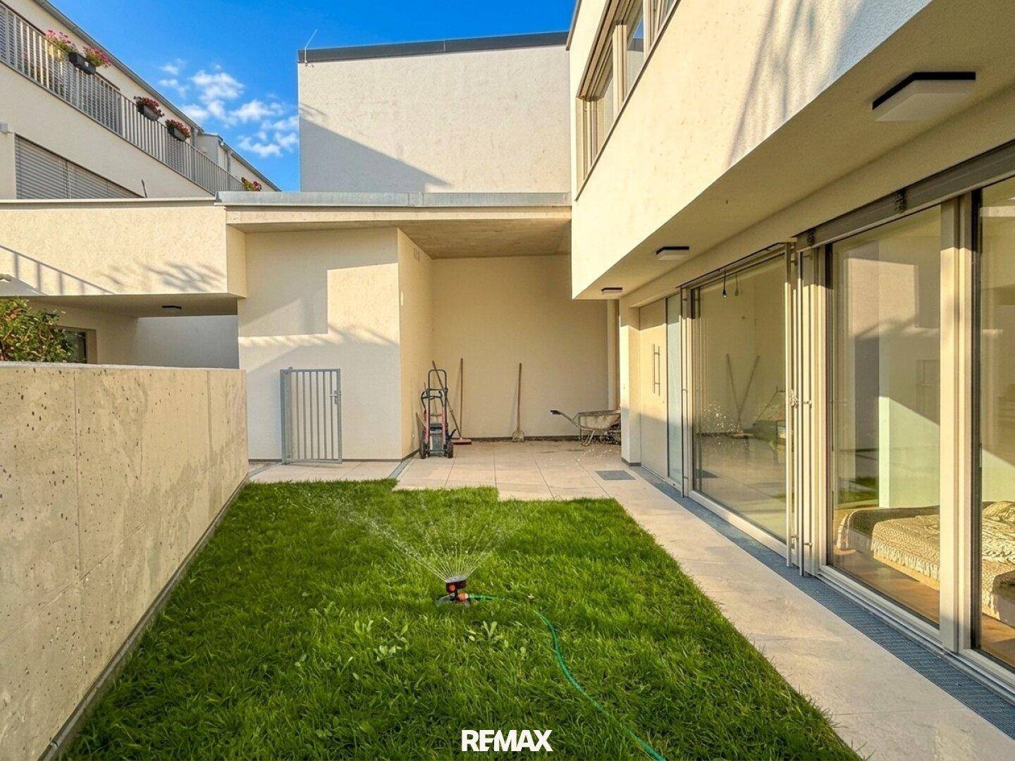 Kleiner, gepflegter Gartenbereich mit Rasen und Bewässerungssystem, angrenzend an die Terrasse.