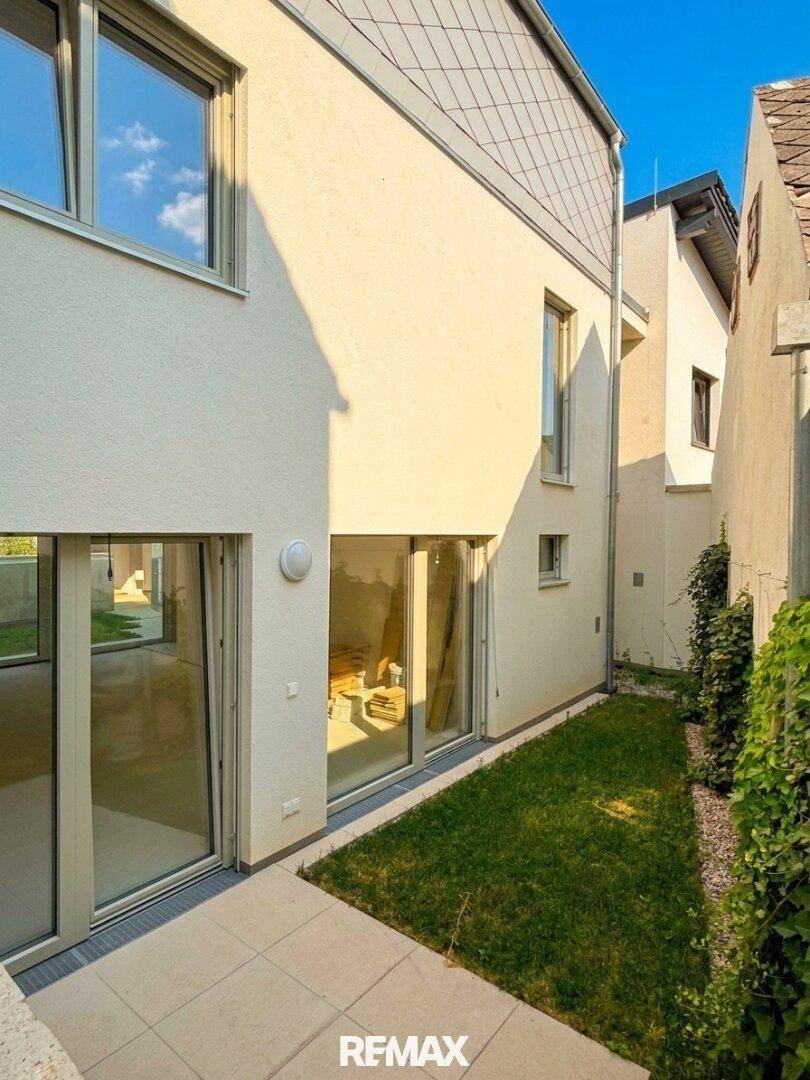Seitlicher Gartenbereich mit Rasen und Kletterpflanzen, angrenzend an die moderne Fassade.