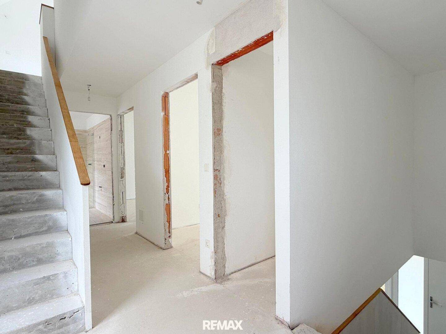 Unfertiger Flur mit Treppe und mehreren Türöffnungen, bereit für den Innenausbau.