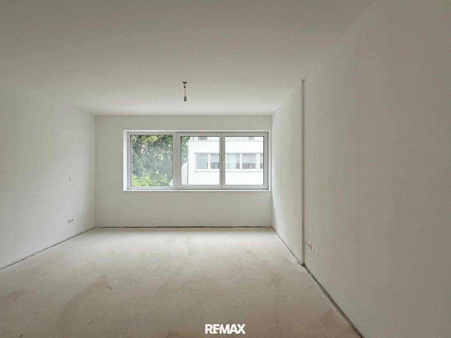 Helles Schlafzimmer im Rohbau mit großem Fenster und Blick auf die Umgebung.