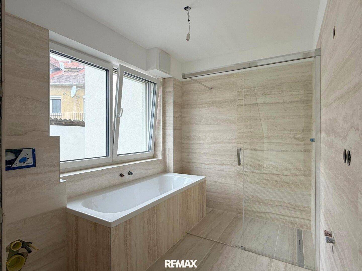 Modernes Badezimmer im Rohbau mit Badewanne, begehbarer Dusche und Fenster.