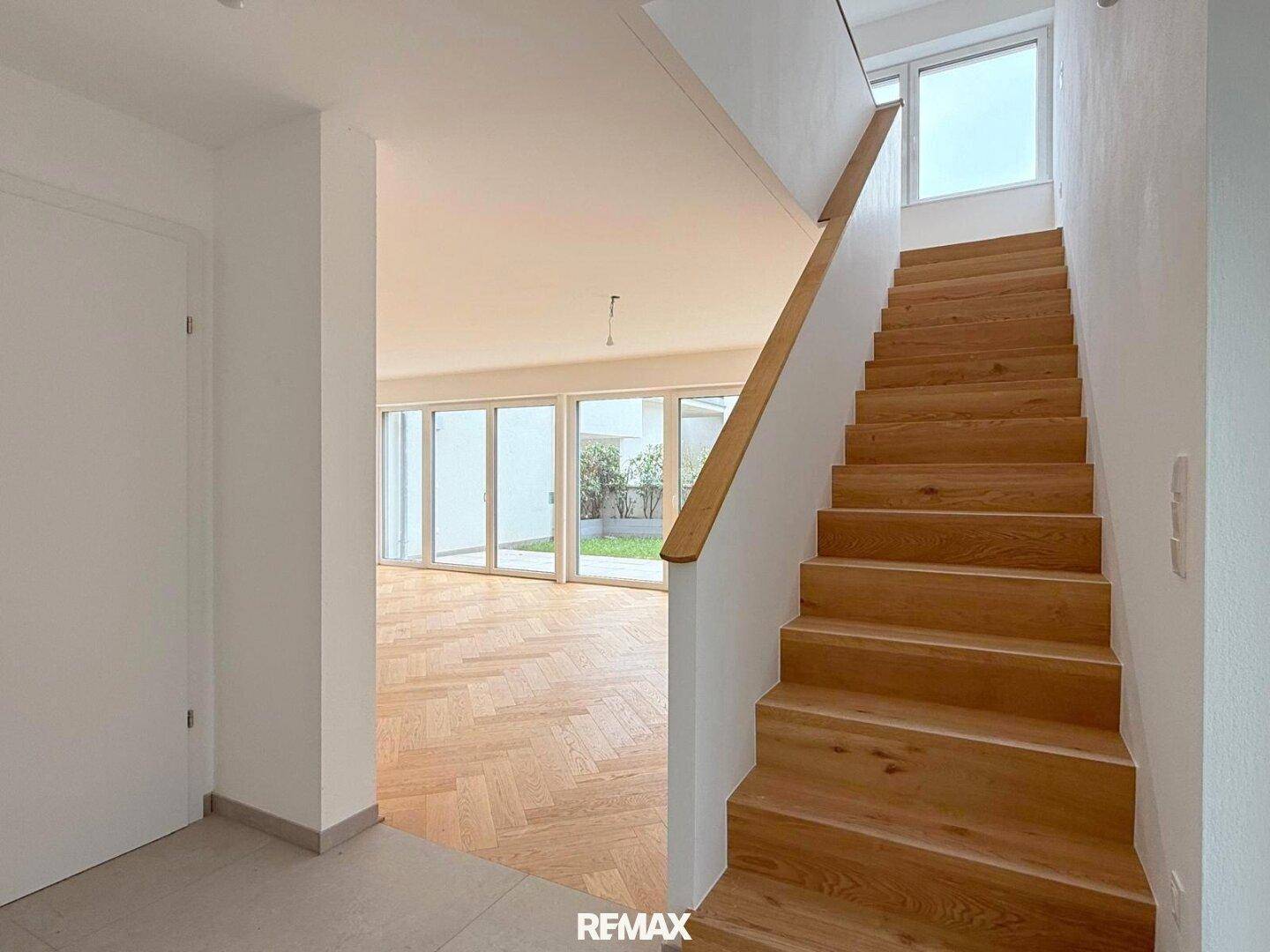 Heller Eingangsbereich mit Holztreppe und Blick in den offenen Wohnbereich mit Parkettboden.