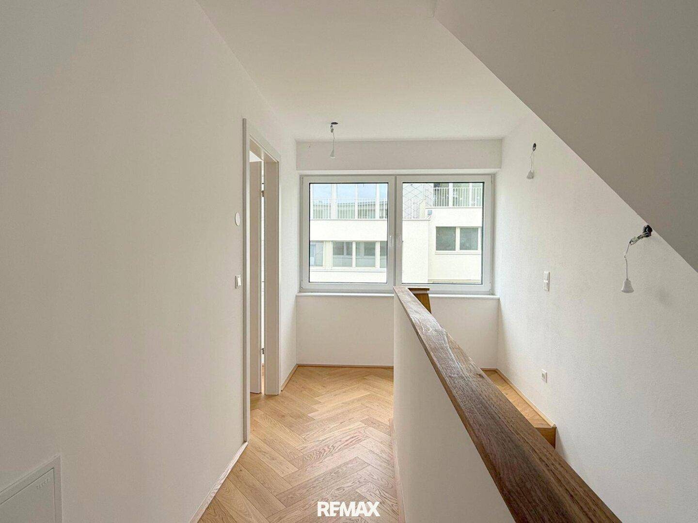 Heller Flur im Obergeschoss mit Parkettboden und einem Fenster, das viel Tageslicht hereinlässt.