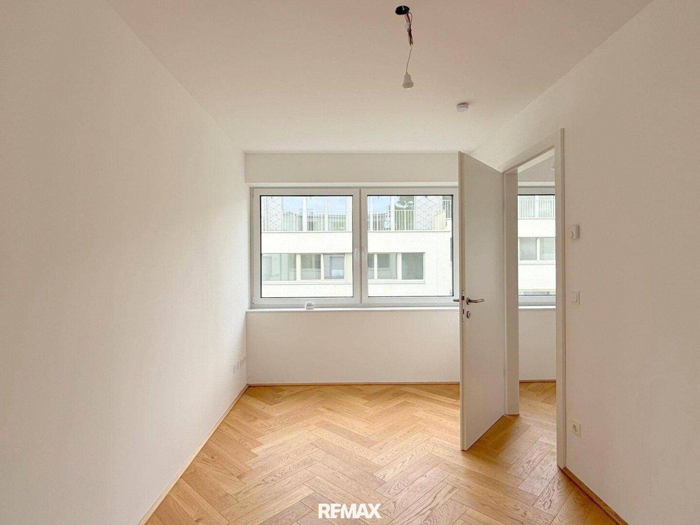 Leeres Schlafzimmer mit Eichenparkett und großen Fenstern, die einen Blick auf die Umgebung bieten.