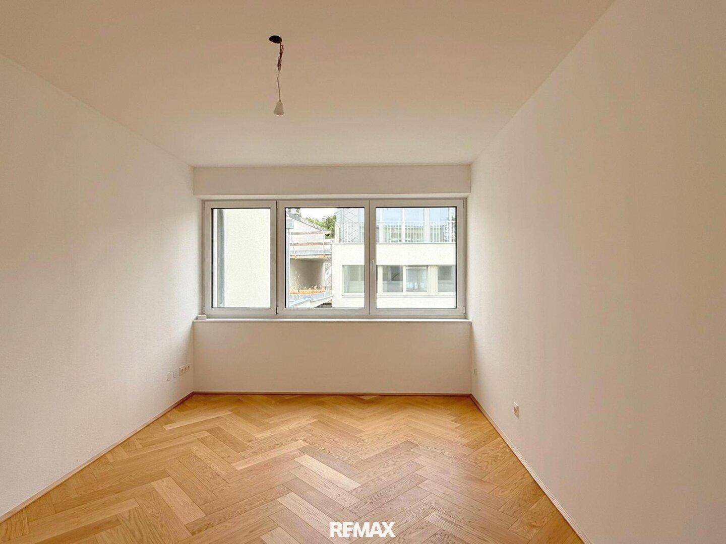 Helles Schlafzimmer mit Fischgrätparkett und breiter Fensterfront, bereit für individuelle Gestaltung.