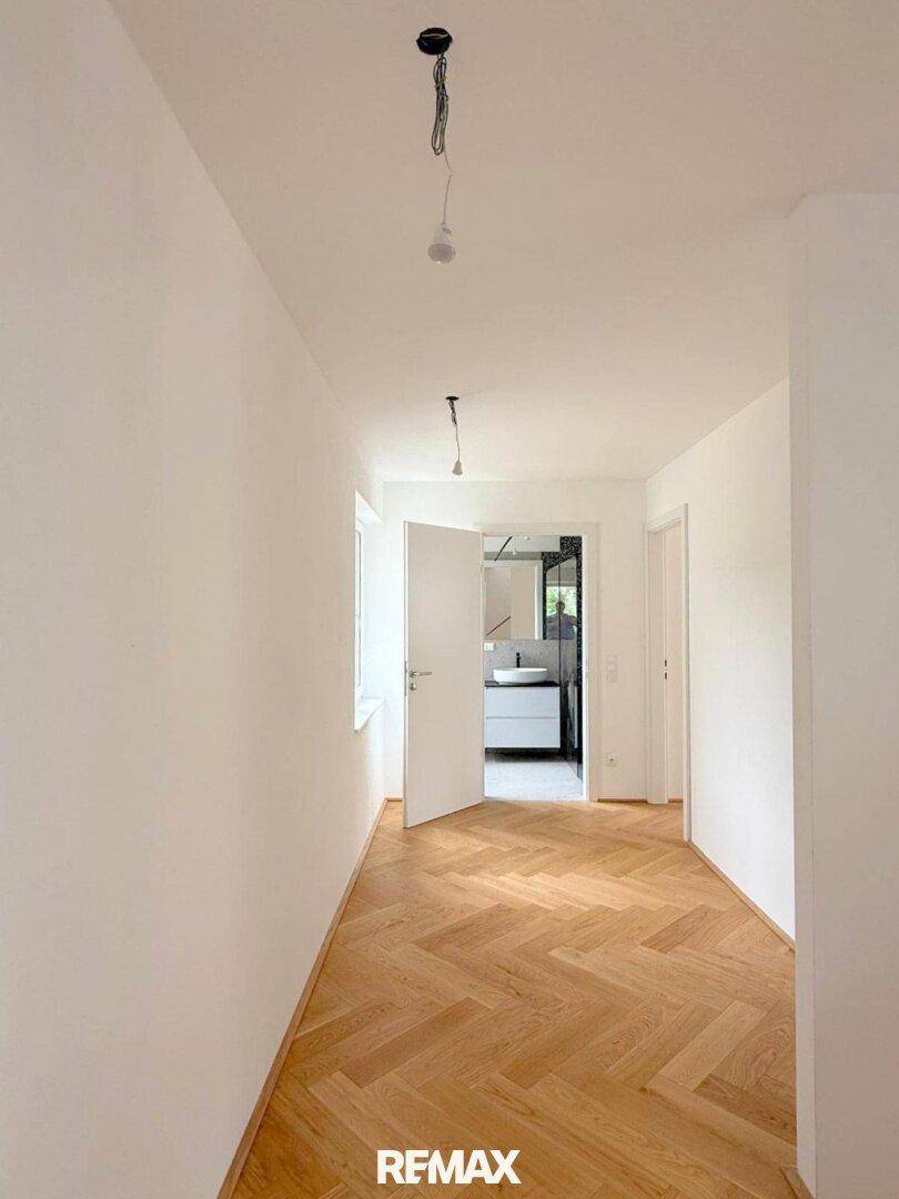 Langer, heller Flur mit Parkettboden, der zu einem modernen Badezimmer führt.