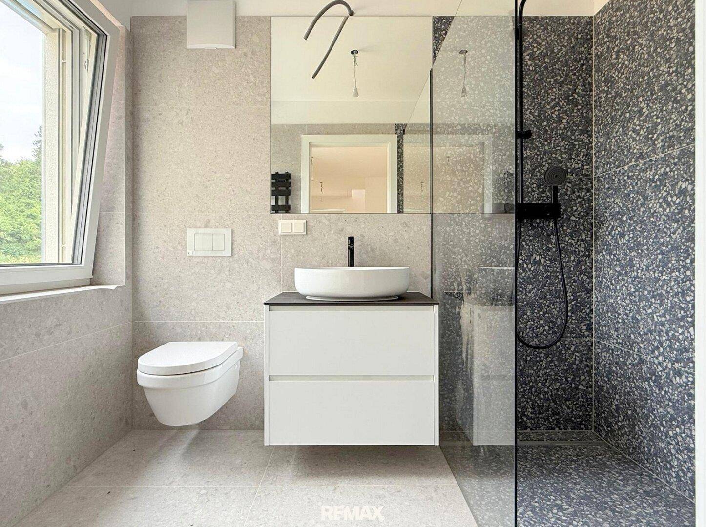 Modernes Badezimmer mit großformatigen Fliesen, wandhängendem WC und ebenerdiger Dusche.