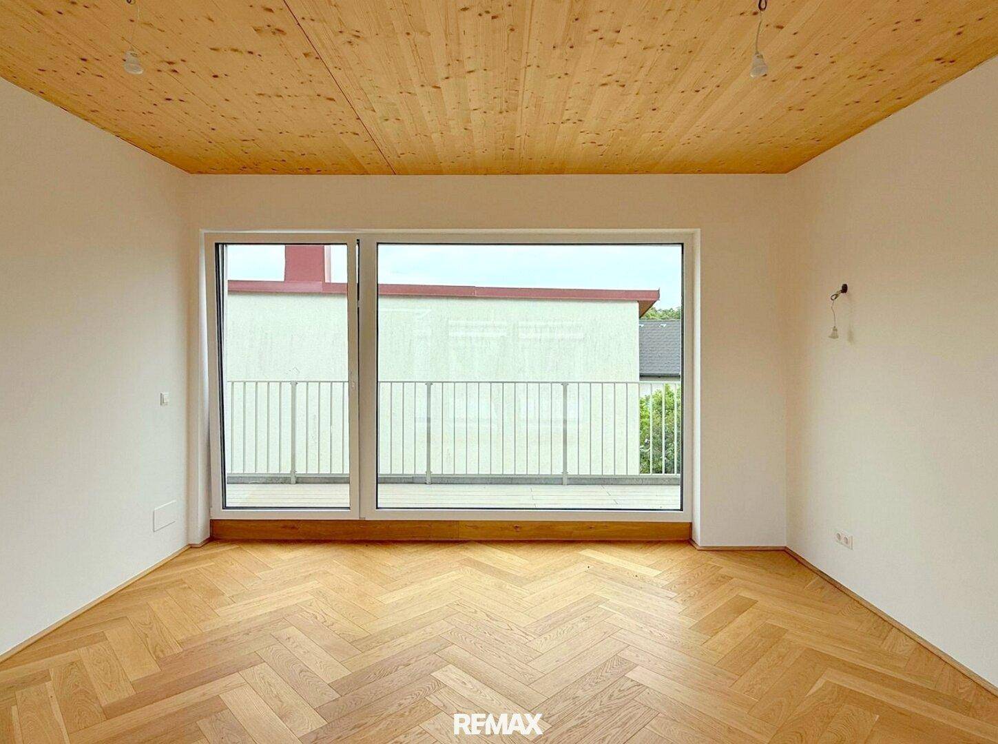 Geräumiges Zimmer mit Holzbalkendecke, Fischgrätparkett und Zugang zu einem Balkon.