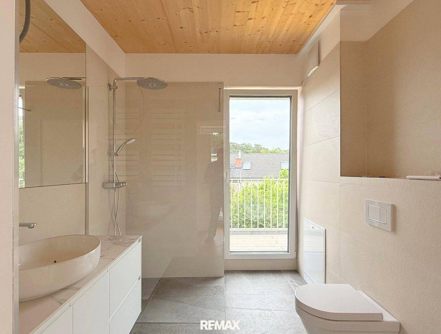 Elegantes Badezimmer mit Holzbalkendecke, modernem Waschtisch und ebenerdiger Dusche mit Balkonzugang.