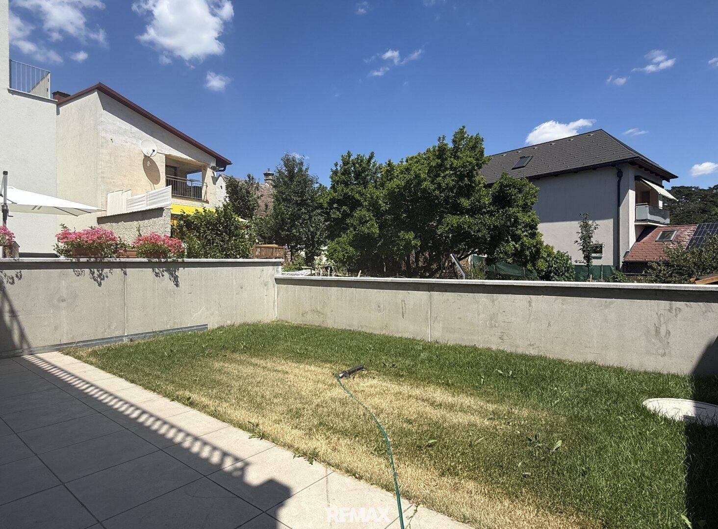Gepflegter Gartenbereich mit Rasenfläche und angrenzender Terrasse, umgeben von weiteren Gebäuden.