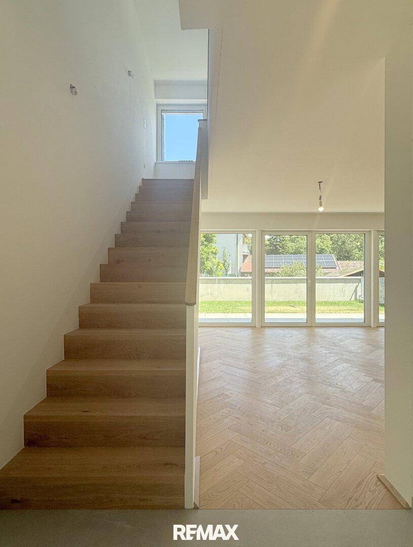Elegante Holztreppe führt in die obere Etage, mit Blick auf den hellen Wohnbereich.