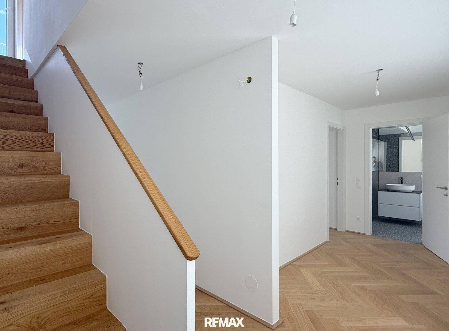 Heller Flur mit Holztreppe und Zugang zu einem modernen Badezimmer.