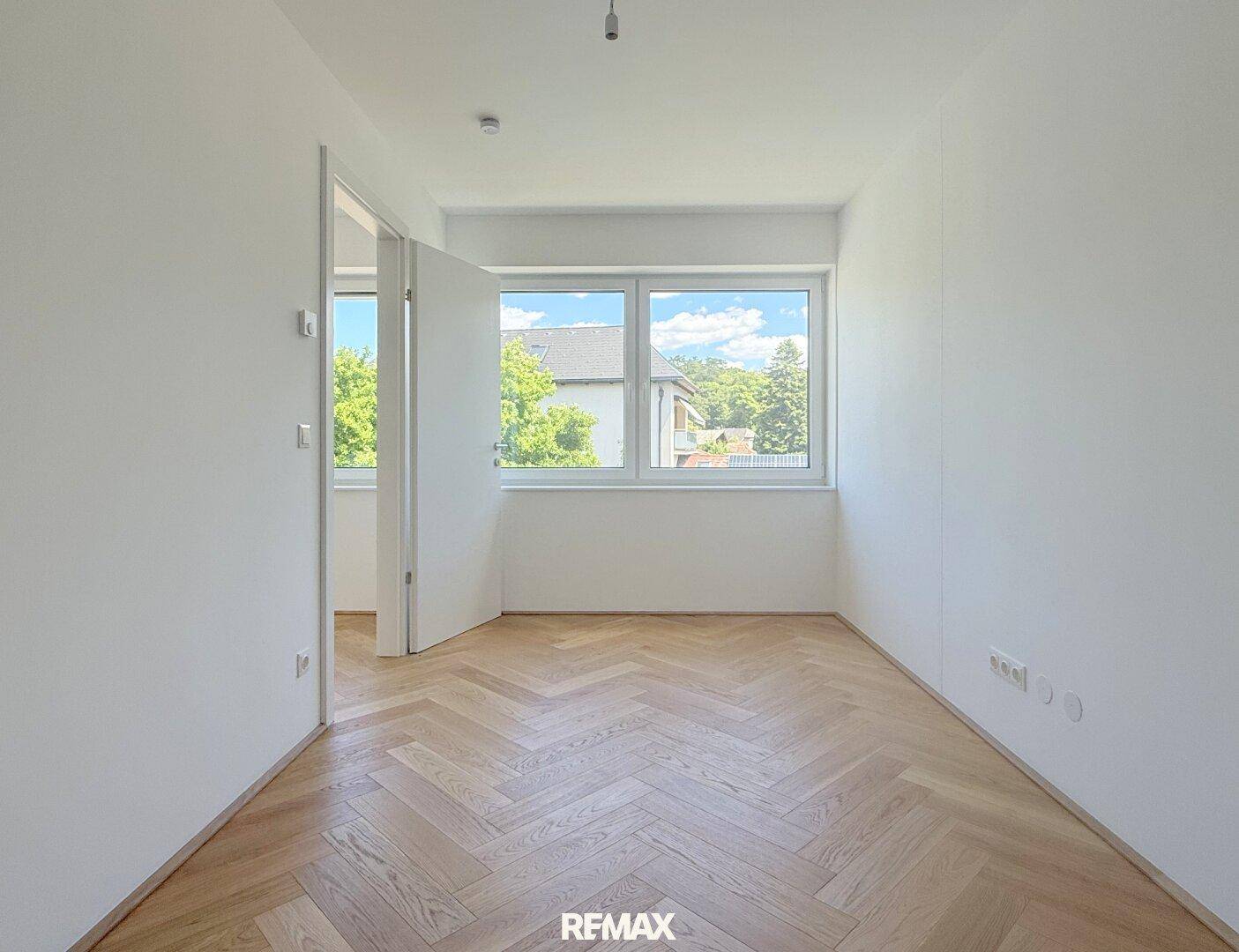 Helles Schlafzimmer mit Fischgrätparkett und Fenstern mit Blick ins Grüne.
