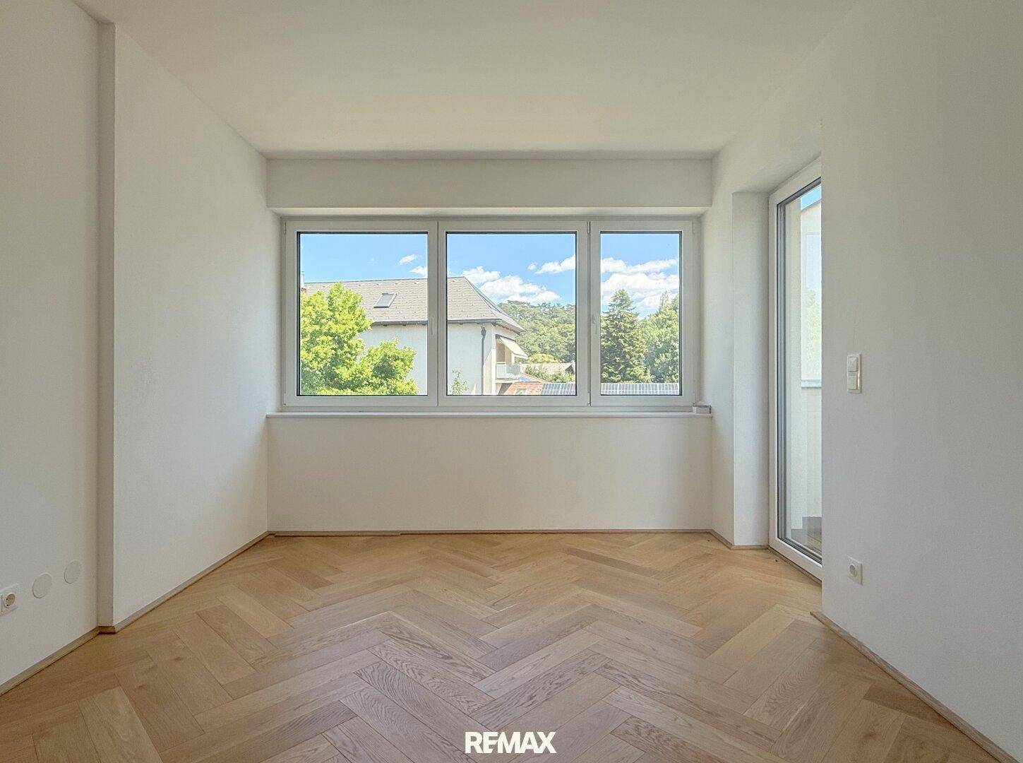 Geräumiges Schlafzimmer mit Fischgrätparkett und Zugang zu einem französischen Balkon.