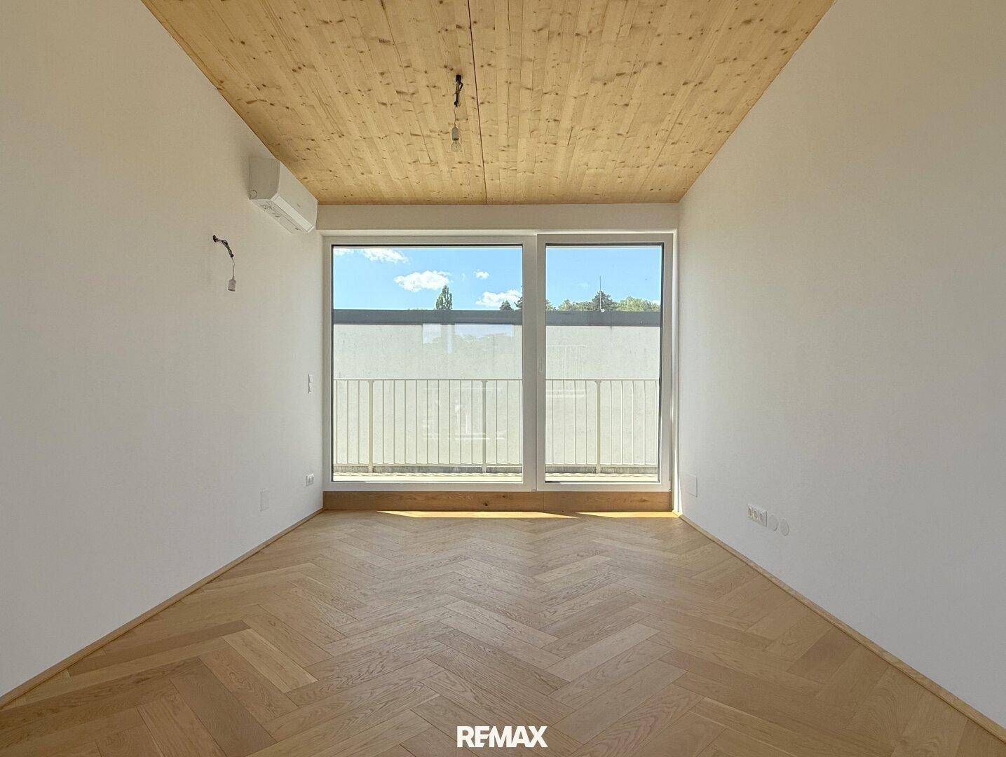 Schlafzimmer mit Holzbalkendecke, Fischgrätparkett, Klimaanlage und Balkonzugang.