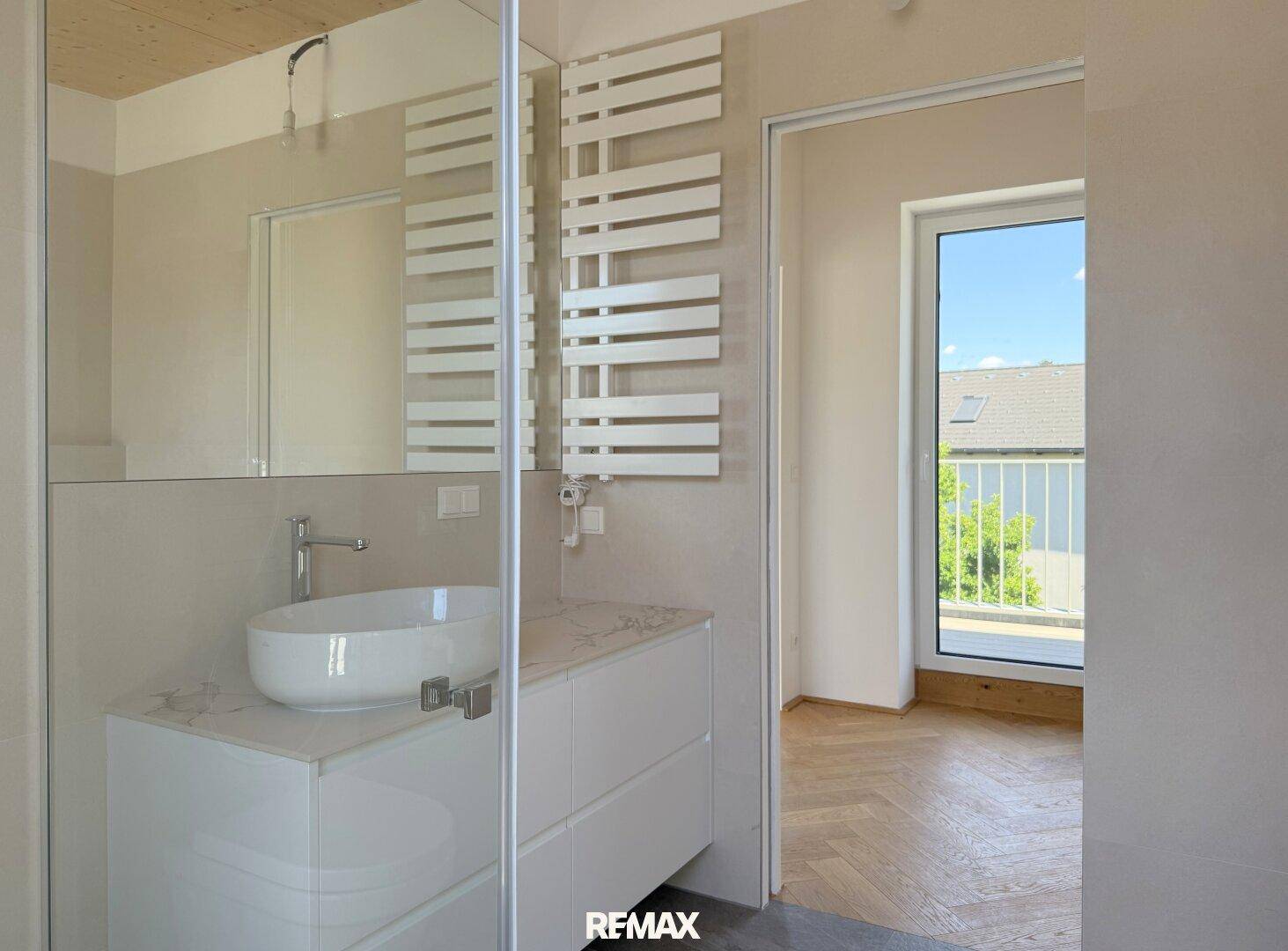 Modernes Badezimmer mit beheiztem Handtuchhalter und Zugang zu einem angrenzenden Raum mit Balkon.