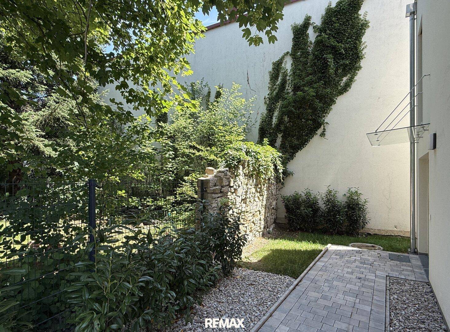 Kleiner, gepflegter Gartenbereich neben dem Gebäude mit üppigem Grün und einer historischen Steinmauer.