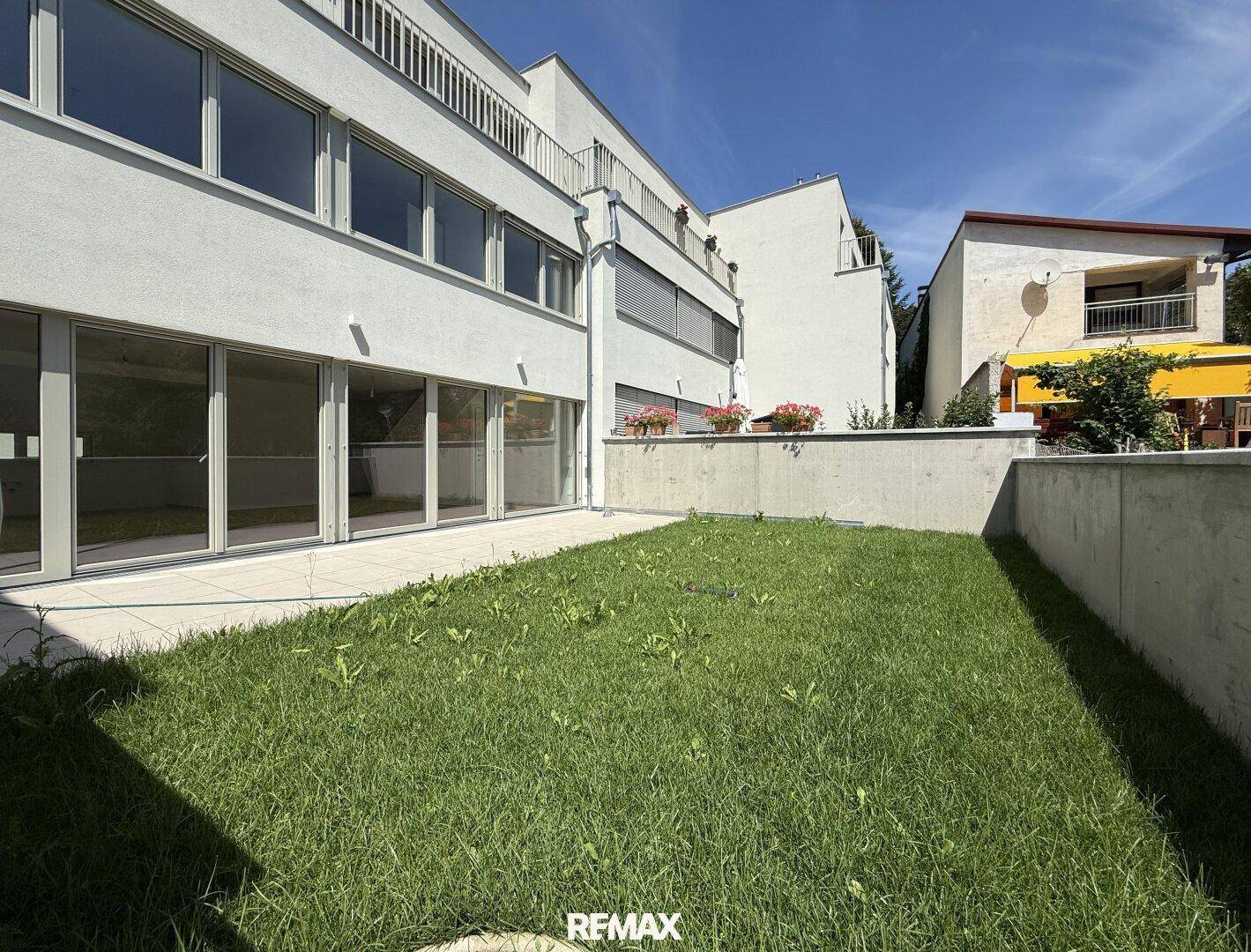 Moderne Gebäudefassade mit privatem Garten und sonniger Terrasse im Erdgeschoss.
