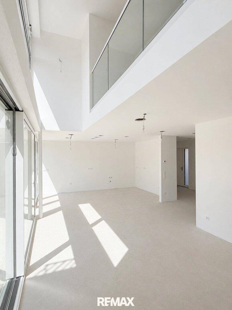 Lichtdurchfluteter Wohnraum mit hohen Decken, Galerie und bodentiefen Fenstern.