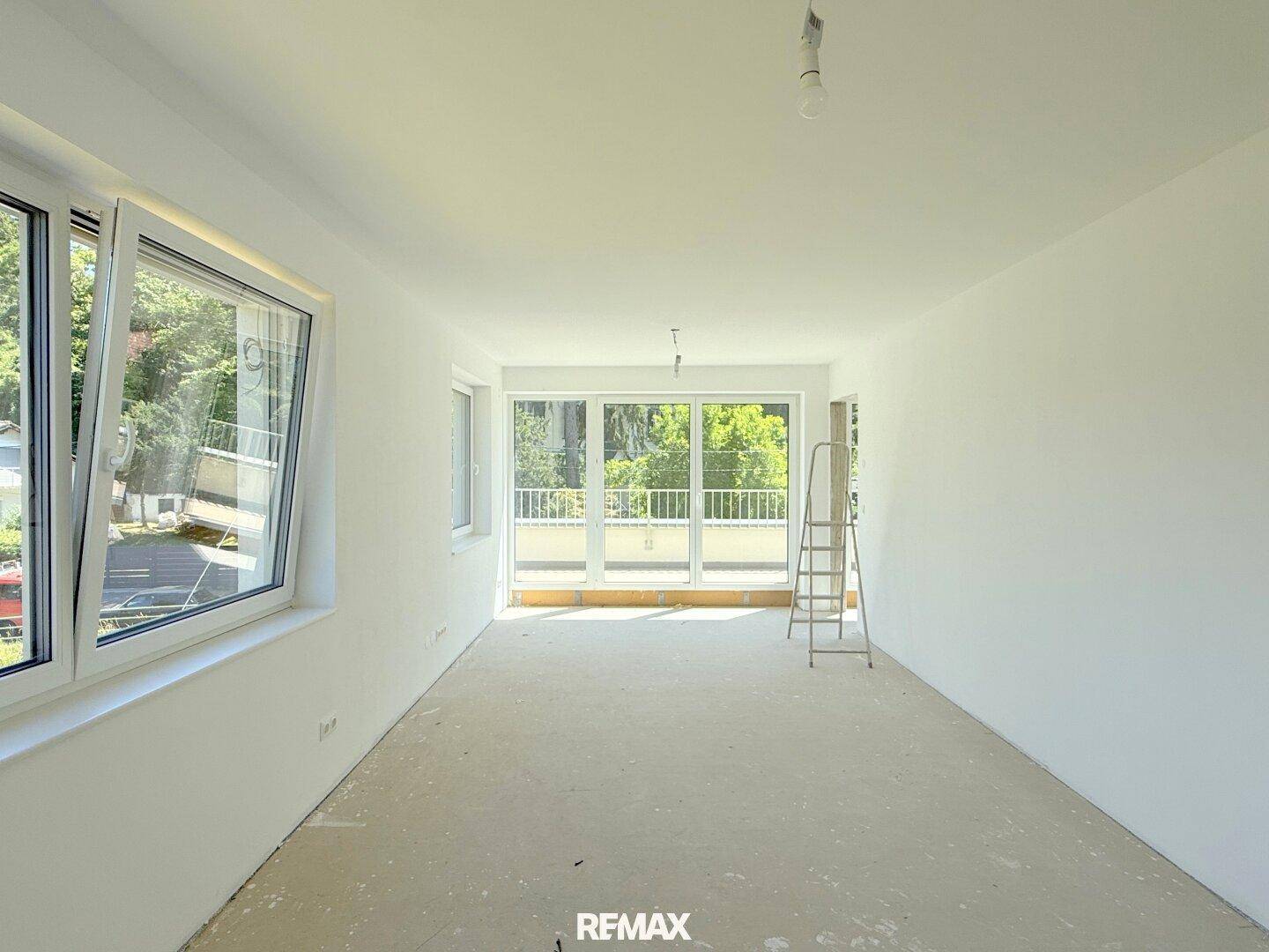 Geräumiger Raum mit Zugang zum Balkon und großen Fenstern, noch im Rohbau.