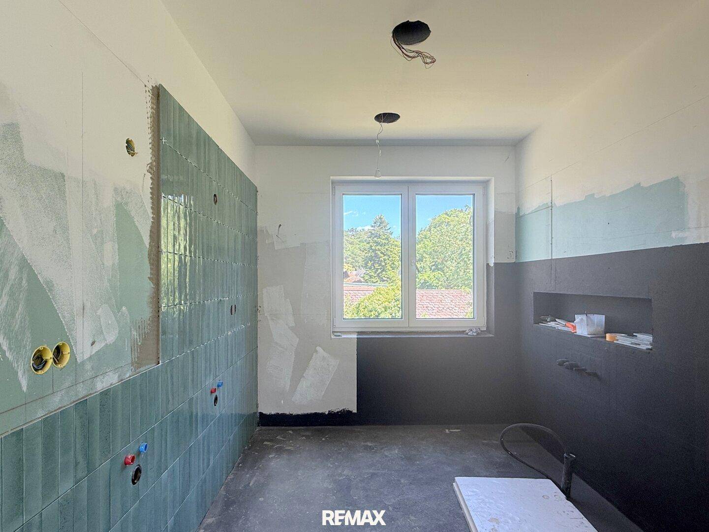 Badezimmer im Rohbau mit modernen grünen Fliesen und Fenster für Tageslicht.