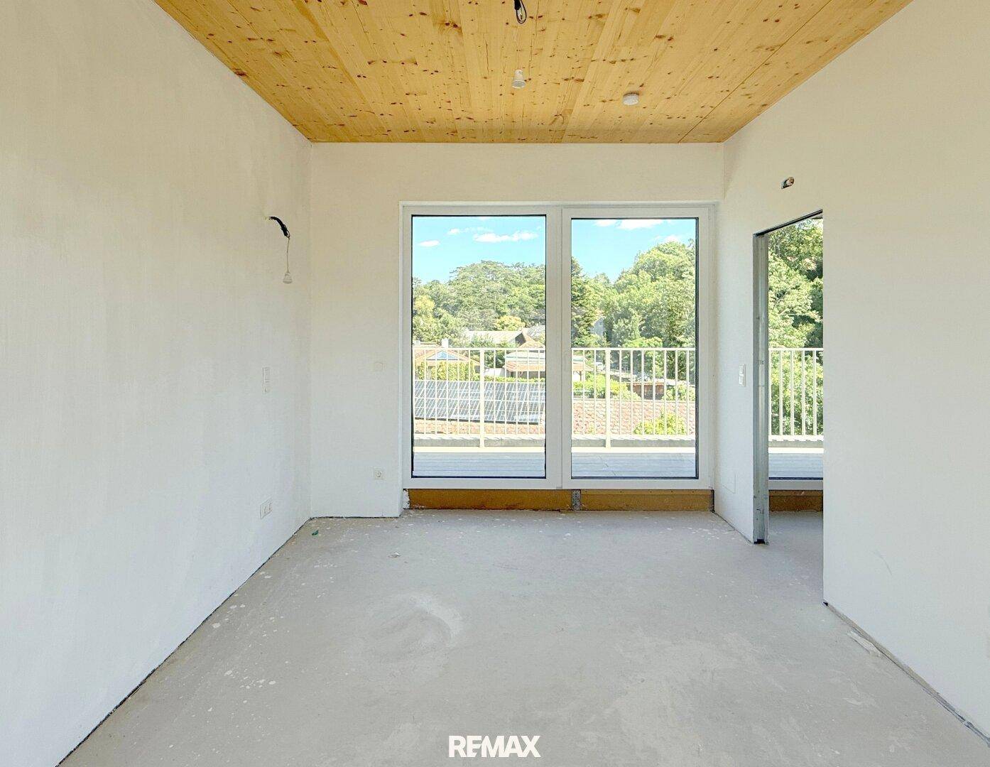 Schlafzimmer mit Holzbalkendecke, Zugang zum Balkon und Blick ins Grüne.