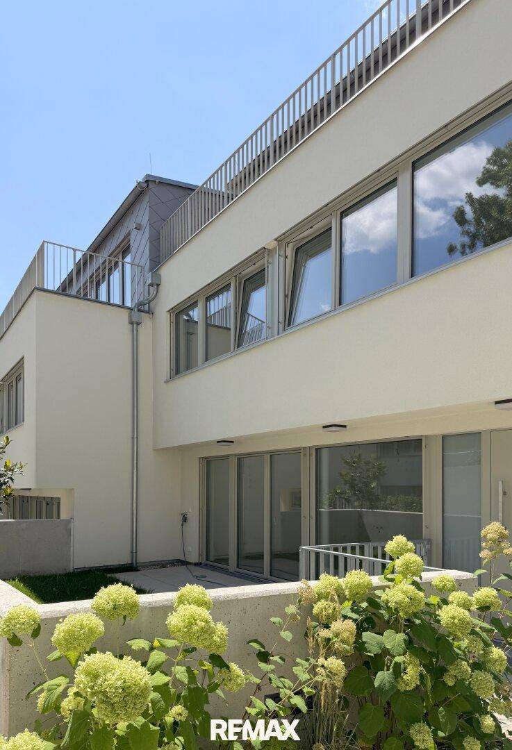 Moderne Wohnanlage mit weißer Fassade, großen Fenstern und gepflegten Grünflächen.