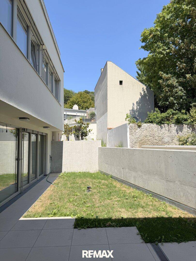 Kleiner privater Gartenbereich mit Rasenfläche und moderner Betonmauer neben dem Gebäude.