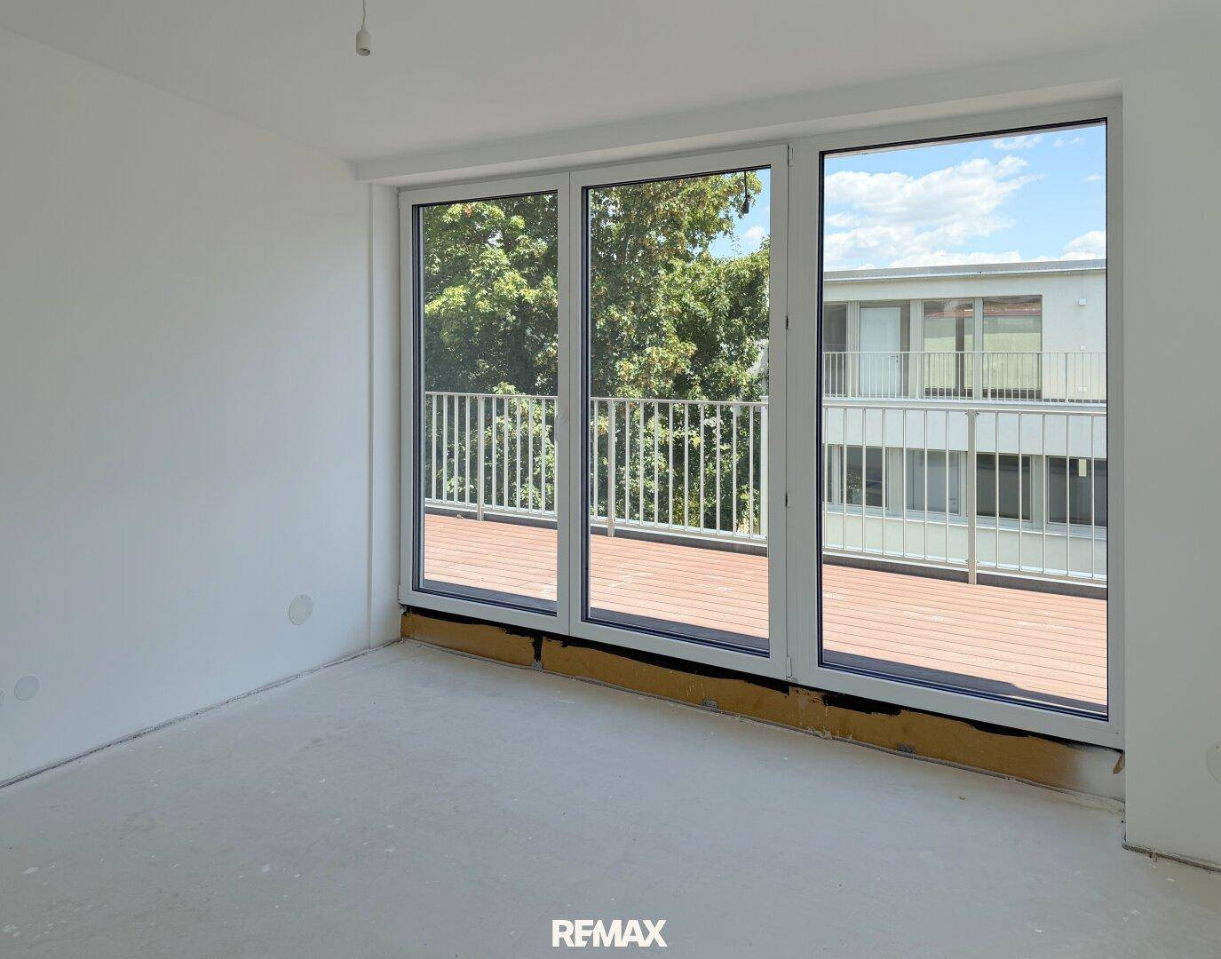 Helles Zimmer im Rohbau mit Zugang zu einem Balkon und Blick auf die Umgebung.