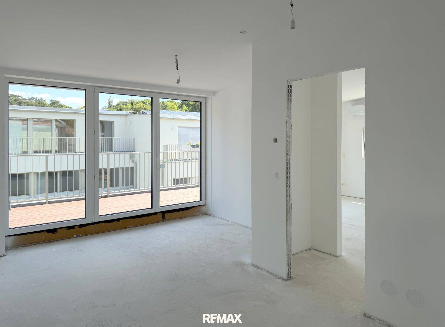 Geräumiges Zimmer im Rohbau mit großen Fenstern und direktem Zugang zum Balkon.