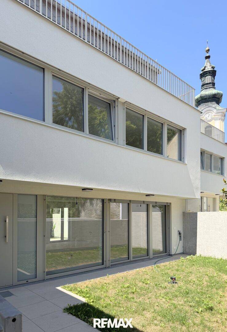 Moderne Gebäudefassade mit großen Fenstern und Zugang zu kleinen Gartenbereichen.