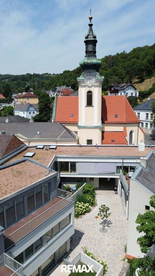 Luftaufnahme einer Kirche mit markantem Turm und umliegenden Gebäuden in einer grünen Landschaft.