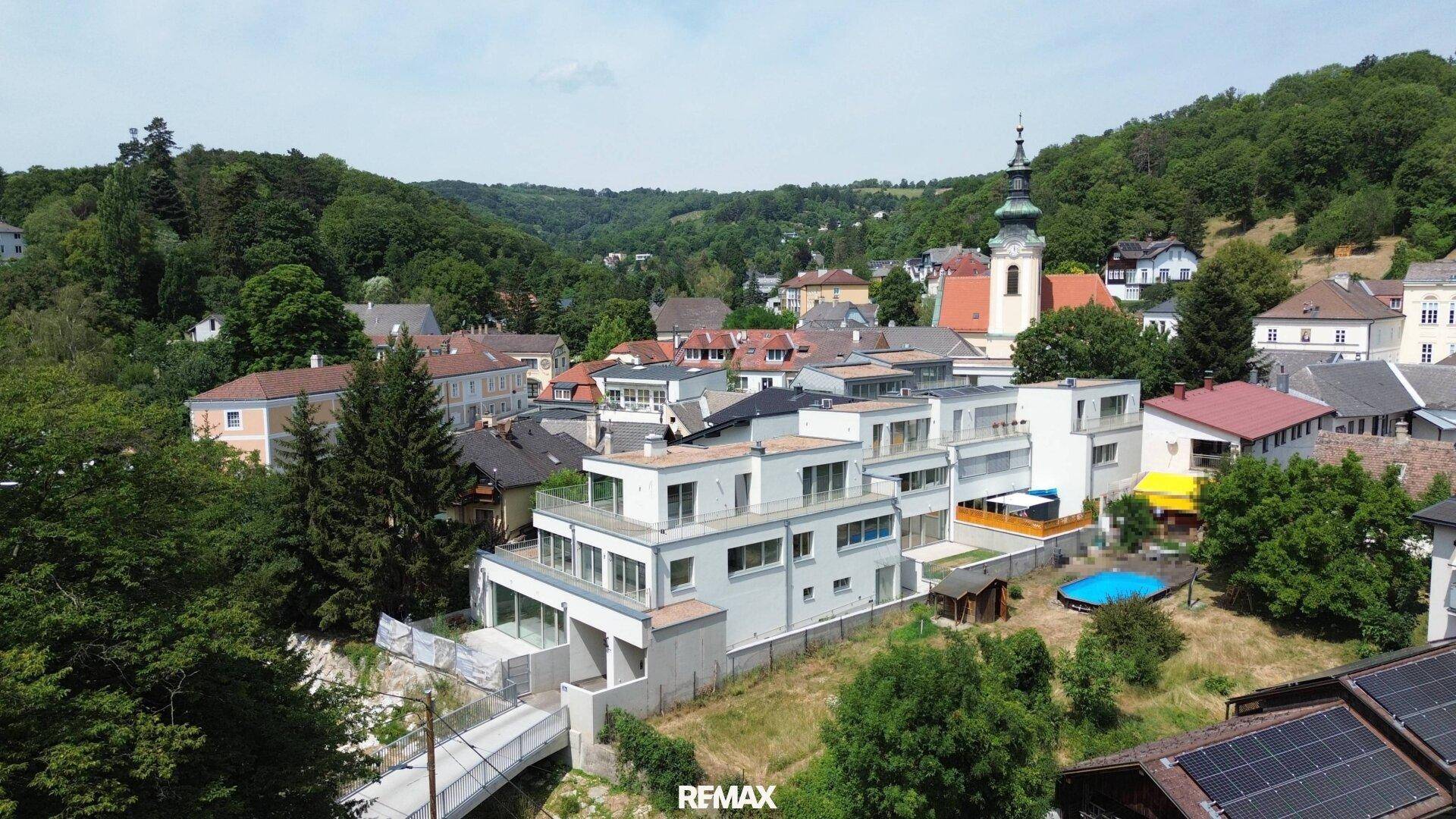Panoramablick auf eine malerische Stadt mit modernen Gebäuden, einer Kirche und bewaldeten Hügeln.